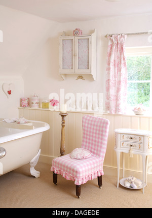 Vérifier la couverture rose lâche sur la chaise à côté de baignoire dans salle de bain pays blanc avec armoire murale et rideaux rose Banque D'Images