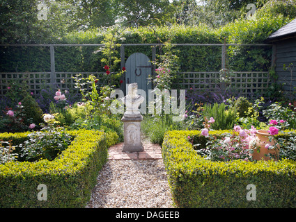 Statue classique dans la base du centre du pays formel jardin avec allée de graviers et de roses dans les lits clos par des haies de faible Banque D'Images