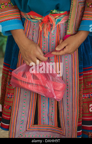 Détail de la femme Hmong Fleur costume tribal distinctif. Saisissant un sac en plastique avec des sandales en plastique. Marché Coc Ly, Vietnam Banque D'Images