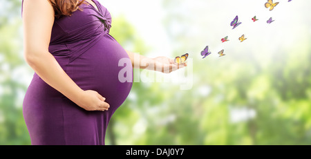 Pregnant woman holding her belly et papillons sur sa main dans un parc Banque D'Images