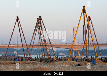 Grues de construction à côté d'un bidonville sur les rives de la rivière Karnaphuli à Chittagong au Bangladesh Banque D'Images