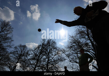 Un joueur de boules métalliques jette sa balle en l'air dans le jardin de la Cour (Hofgarten) à Munich, Allemagne, 29 mars 2011. La hausse des températures a attiré les gens à visiter les jardins de la capitale de l'état bavarois. Photo : PETER KNEFFEL Banque D'Images