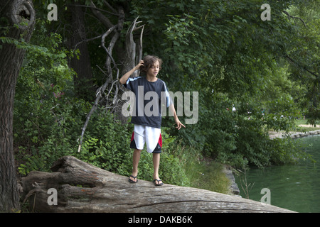 Garçon sur une grande marche soigneusement tronc de l'arbre qui tombe dans l'eau sur le lac à Prospect Park, Brooklyn, New York. Banque D'Images