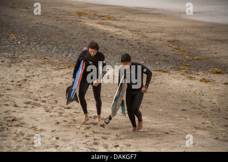 Le port de combinaisons et l'exécution des planches, deux adolescent membres de l'équipe de surf de l'école secondaire à pied à travers la ville's beach. Banque D'Images