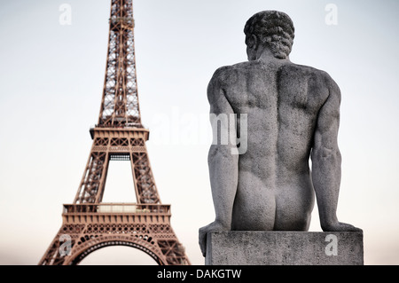 Paris France Tour Eiffel close-up avec statue de pierre de l'homme assis à l'arrière à ciel au crépuscule Banque D'Images