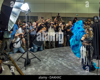 Sous l'éclairage de studio, les photographes amateurs foule photographier un modèle pendant une séance de photo à un salon photographique. Banque D'Images