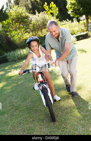 Older Man teaching petite-fille à circuler à bicyclette Banque D'Images