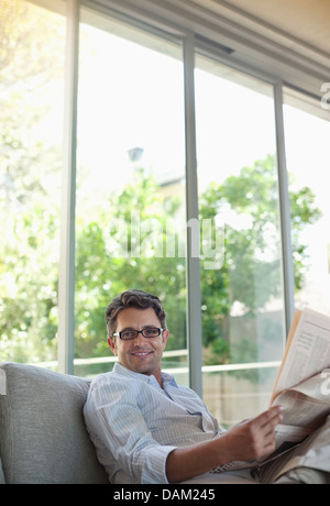 Man reading newspaper on sofa Banque D'Images