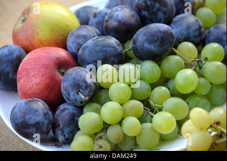 Les prunes, pommes et raisins sur une plaque Banque D'Images