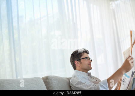 Man reading newspaper on sofa Banque D'Images