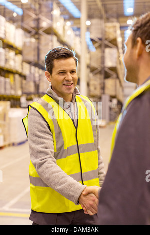 Workers shaking hands in warehouse Banque D'Images