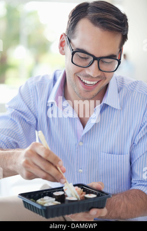 Businessman eating sushi in office Banque D'Images