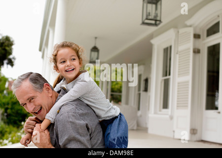Homme plus âgé portant sa petite-fille piggy back on porch Banque D'Images