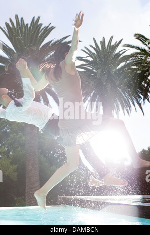 En tenue couple jumping into swimming pool Banque D'Images