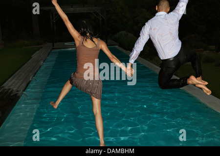 En tenue amis jumping into swimming pool Banque D'Images