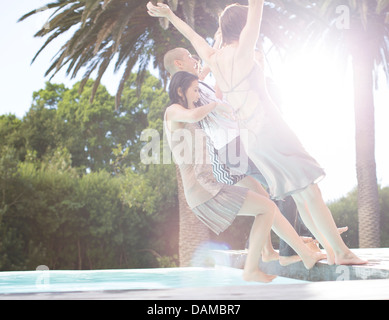 En tenue amis jumping into swimming pool Banque D'Images