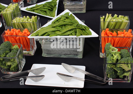 Arrangement tentant de légumes frais dans des bols en verre avec des pinces sur plaque blanche,une nappe noire utilisée comme arrière-plan. Banque D'Images