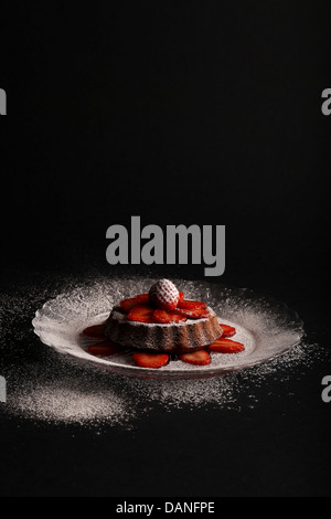 Vanille citron gâteau mini avec fraise sur le dessus et les fraises tranchées sur plaque de verre et fond sombre. Banque D'Images