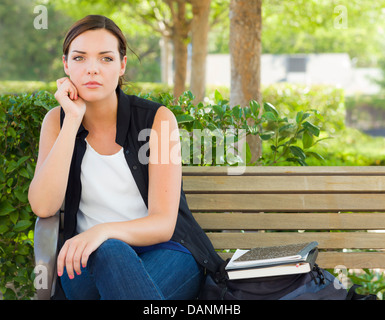 Mélancolie Jeune Adulte femme assis sur un banc à côté de livres et de sac à dos. Banque D'Images