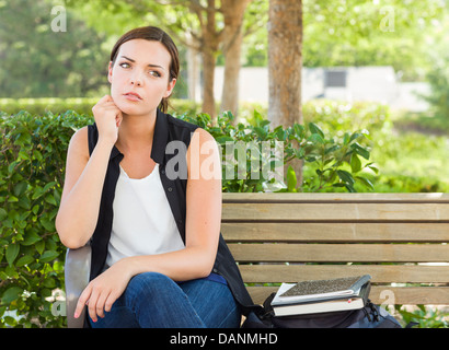 Mélancolie Jeune Adulte femme assis sur un banc à côté de livres et de sac à dos. Banque D'Images