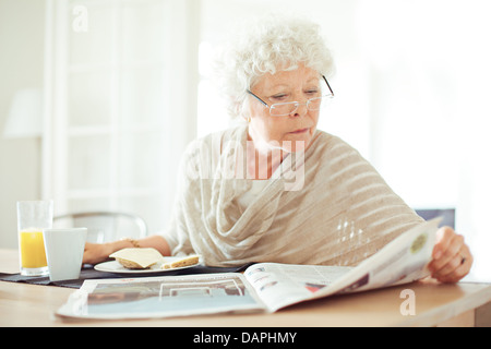 La haute atmosphère femme qui a son petit-déjeuner et la lecture les nouvelles du matin Banque D'Images