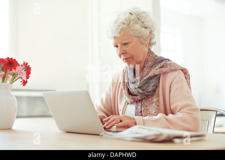Femme âgée à la maison tapant quelque chose en utilisant son ordinateur portable Banque D'Images