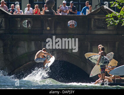 Un jeune homme sur son surf saute par dessus l'Eisbach 'Wave' sur l'Eisbach river au jardin anglais à Munich, Allemagne, 23 août 2011. Sur la droite, d'autres internautes attendent leur tour. Les passants regarder le surfeur du pont. Le vague à l'Eisbach Prinzregenten Street est un lieu célèbre pour les surfeurs et les sportifs de l'eau toute l'année. Photo : Peter Kneffel Banque D'Images