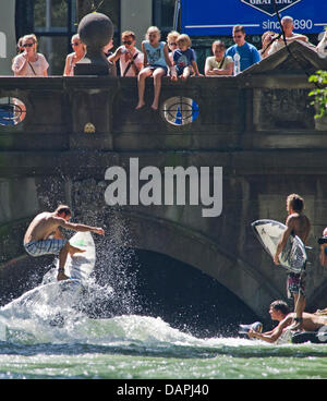 Un jeune homme sur son surf saute par dessus l'Eisbach 'Wave' sur l'Eisbach river au jardin anglais à Munich, Allemagne, 23 août 2011. Sur la droite, d'autres internautes attendent leur tour. Les passants regarder le surfeur du pont. Le vague à l'Eisbach Prinzregenten Street est un lieu célèbre pour les surfeurs et les sportifs de l'eau toute l'année. Photo : Peter Kneffel Banque D'Images