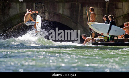 Un jeune homme sur son surf saute par dessus l'Eisbach 'Wave' sur l'Eisbach river au jardin anglais à Munich, Allemagne, 23 août 2011. Sur la droite, d'autres internautes attendent leur tour. Les passants regarder le surfeur du pont. Le vague à l'Eisbach Prinzregenten Street est un lieu célèbre pour les surfeurs et les sportifs de l'eau toute l'année. Photo : Peter Kneffel Banque D'Images