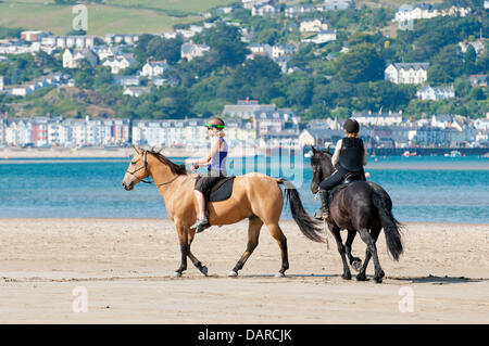 L'estuaire de Dovey/Borth, Ceredigion, pays de Galles, Royaume-Uni. 17 juillet 2013. Deux femmes montent leurs chevaux sur le sable. Une étendue de sable plat dur-qui offre un immense parking pour les voitures à 1 € par voiture par jour - dans la Dovey Dyfi (en gallois) Estuaire, fait partie d'une grande surface des eaux côtières soutenue par la campagne du Pays de Galles et du Conseil ainsi que les dunes de sable environnantes offre un magnifique salon pour les gens d'échapper à la vague de chaleur qui a été la Grande-Bretagne torride pendant près de deux semaines. L'accueil cool brise de mer soufflent en provenance de la mer d'Irlande. Crédit photo : Graham M. Lawrence/Alamy Live News. Banque D'Images