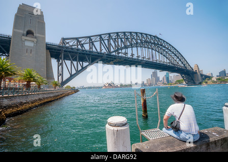 Un touriste est assis seul sur la station d'Millsons Point profiter de la vue de l'emblématique pont du port de Sydney Banque D'Images