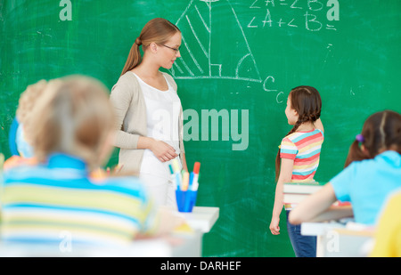 Portrait de smart teacher standing by blackboard et regardant cute girl solution expliquant Banque D'Images