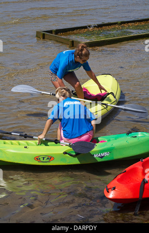 Deux jeunes femmes portant les T-shirts de l'Académie des sports nautiques d'entrer dans des kayaks à colorées, Sandbanks Poole, Dorset en Juillet Banque D'Images