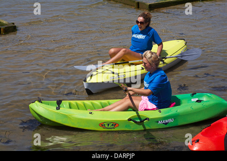 Deux jeunes femmes portant les T-shirts de l'Académie des sports nautiques d'entrer dans des kayaks à colorées, Sandbanks Poole, Dorset en Juillet Banque D'Images