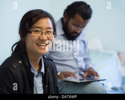 Portrait d'une femme asiatique smiling en premier plan comme un indien utilise une tablette dans l'arrière-plan Banque D'Images