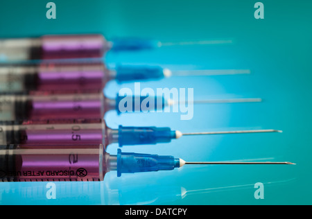 Cinq injections des seringues en plastique remplie de liquide rose sur le tableau bleu portant dans une rangée Banque D'Images