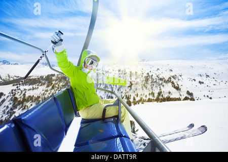 Happy young woman skieur assis sur la chaise de ski, souriant et heureux de lever ses mains Banque D'Images