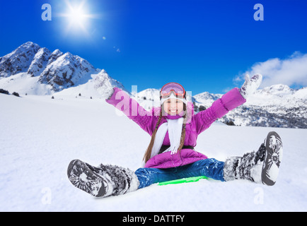 Happy girl faisant glisser sur un traîneau avec ses mains levées, le port de masque de ski, dans les montagnes Banque D'Images