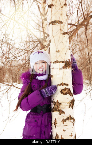 Cute little girl hugging il bouleau sur neige de l'hiver 24 Banque D'Images