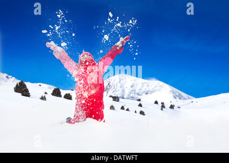 Peu d'happy smiling girl projette la neige dans l'air avec des flocons de voler dans toutes les directions Banque D'Images