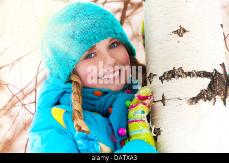 Portrait de petite fille mignonne se cacher derrière le bouleau sur neige de l'hiver 24 Banque D'Images