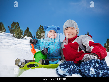 Deux frères assis sur la neige et jouer ensemble sur la journée d'hiver Banque D'Images