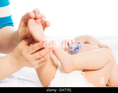 Baby foot massage mère avec ses mains avec bébé allongé sur le lit sur le contexte Banque D'Images