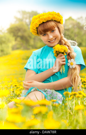 Belle 10 ans fille blonde assise dans le parc avec bouquet de pissenlits Banque D'Images