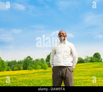 Plaisir certain rire homme noir portant shirt debout à l'extérieur dans le parc sur le champ de pissenlit jaune Banque D'Images