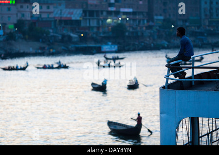 Un homme lance montres et les traversiers de passagers à prendre et de Sadarghat sur la rivière Buriganga à Dhaka, Bangladesh au crépuscule Banque D'Images