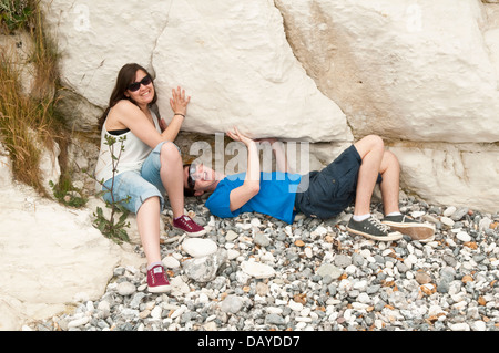 Happy young couple en fin d'adolescence ou au début de la vingtaine sur une plage prétendant rocks tombent sur eux Banque D'Images