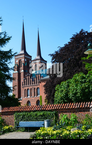 Vue sur la Cathédrale de Roskilde au Danemark avec un banc et fleurs jaune Banque D'Images