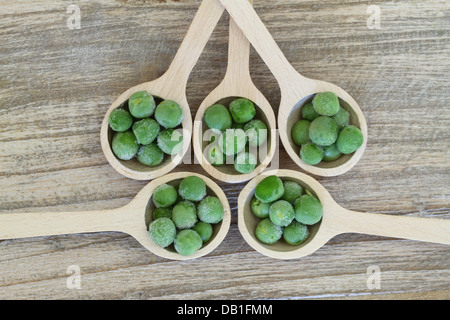 Pois verts congelés sur des cuillères en bois Banque D'Images