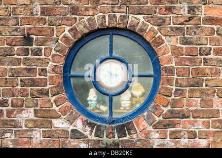 Fenêtre ronde avec l'horloge dans le centre et les nains de jardin à la fenêtre de sortie. UK Banque D'Images
